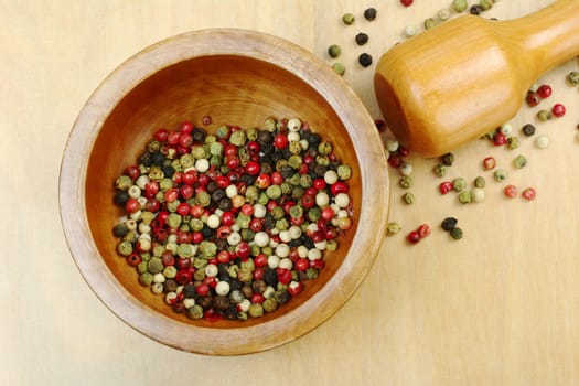 Black, red, green and white peppercorns in wooden mortar with pestle on wooden board photographed from above (Selective Focus, Focus on the peppercorns in the mortar)