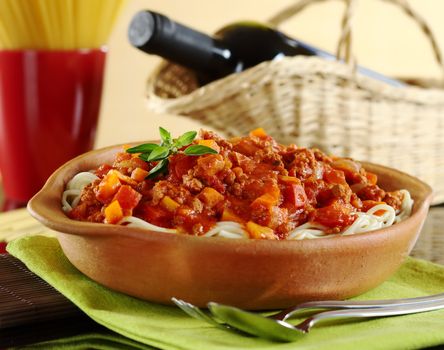 Spaghetti bolognaise with cutlery, a red wine bottle and spaghetti in the background (Selective Focus, Focus on the oregano leaves on the spaghetti)