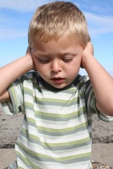 Young blond boy at the beach, closing his ears