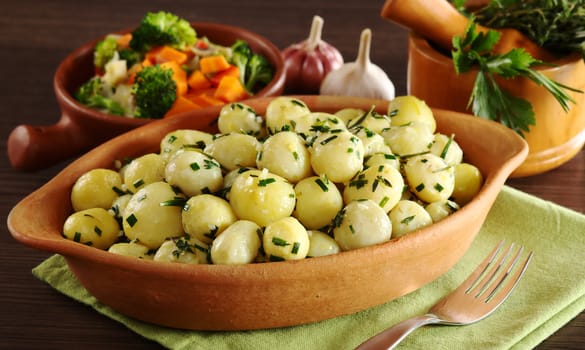 Small potatoes with herbs, such as parsley, thyme and rosemary with vegetables, garlic and a mortar with herbs in the background (Selective Focus, Focus on the front of the potatoes and the bowl)