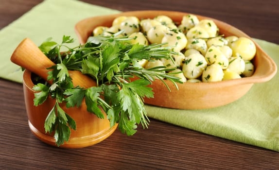 Herbs in wooden mortar (parsley, rosemary) with a potato dish in the background (Shallow Depth of Field, Focus on some of the herbs in the foreground)