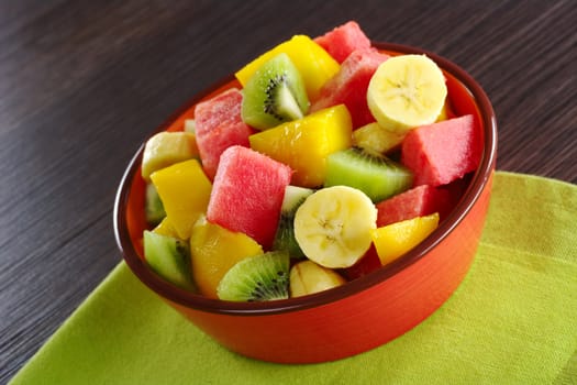 Fresh fruit salad made of banana, kiwi, watermelon and mango pieces in orange bowl (Selective Focus, Focus on the front of the bowl and the fruits in the front)