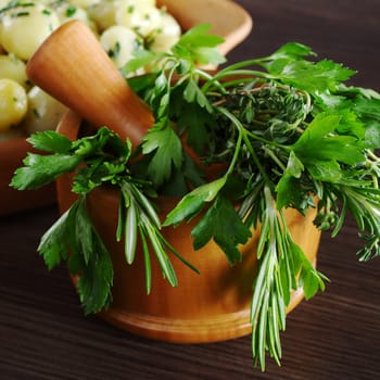 Fresh herbs (parsley, rosemary and thyme) in wooden mortar with pestle (Selective Focus, Focus on the front of the herbs)