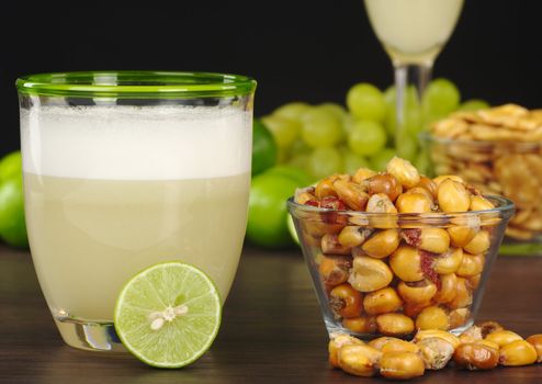 The Peruvian cocktail, Pisco Sour with the Peruvian snack, roasted corn, called cancha and grapes, limes, Pisco Sour and habas (Peruvian roasted beans) in the background (Selective Focus, Focus on the front) 