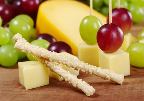 Sesame sticks with cheese and red and white grapes on wooden board (Selective Focus, Focus on the upper sesame stick)