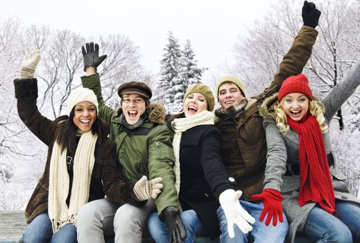 Group of excited young friends with arms raised outdoors in winter