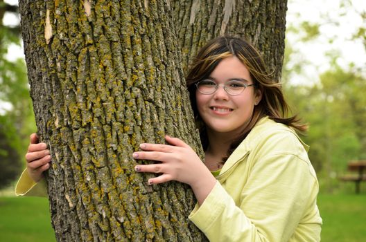 A smiling young girl is hugging a tree.