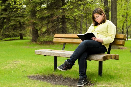 A young girl is sitting on a bench, reading a good book.