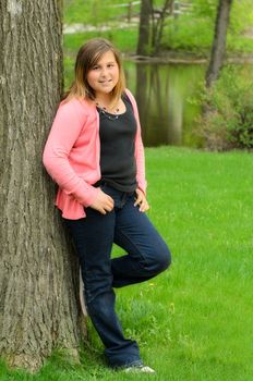 A young girl leaning against a tree with a creek in the background.