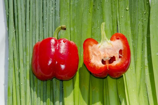 Two fat red paprikas on the row of green orions. One of them cut in a half.