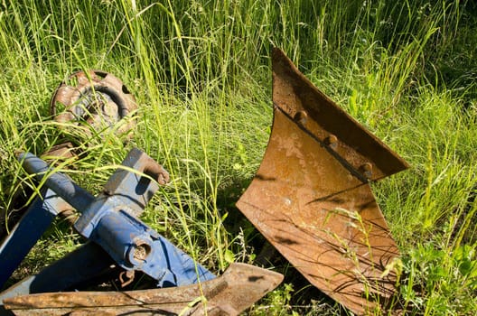 Plough - agricultural tool atachable to tractor for arable. Rusty metal in a long grass.