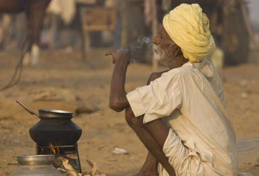 Old man smoking next to his camp fire at the annual Pushkar Camel Fair in Rajasthan, India