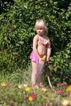 little girl with hosepipe watering flowers
