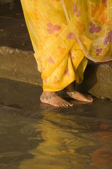 Woman in yellow sari standing on steps by rivers edge. Varanasi Uttar Pradesh India