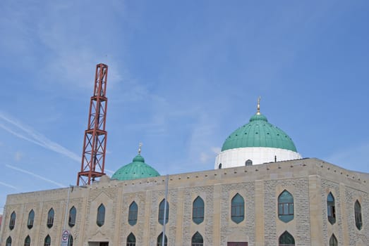 The Green Domes and Minaret of a modern Mosque in a mill town in West Yorkshire under a blue sky