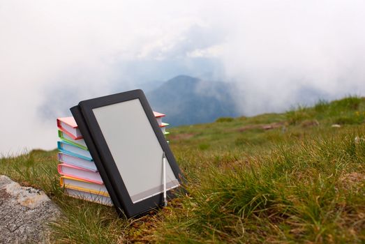 Stack of colorful books and electronic book reader on the grass