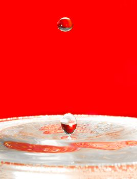 Extreme close-up. Falling droplets of water over red.