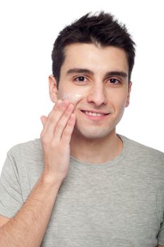 handsome young man applying cream lotion on face (isolated on white background)