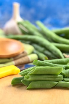 Raw cut green bush beans on wooden board with a kitchen knife, bean pods and garlic in the back (Selective Focus, Focus on the three beans lying on each other) 