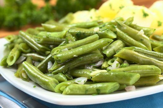 Cooked green beans with onion and parsley with cooked potato in the back (Selective Focus, Focus one third into the beans)