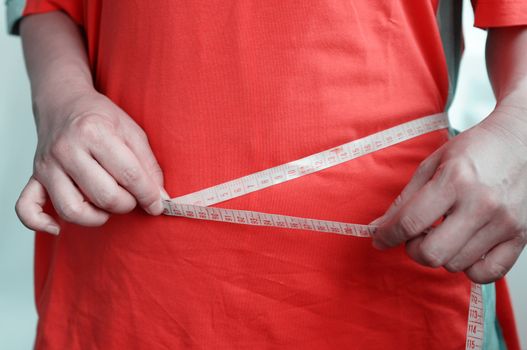 A fat young woman in red clothes measuring her waist with tape measure