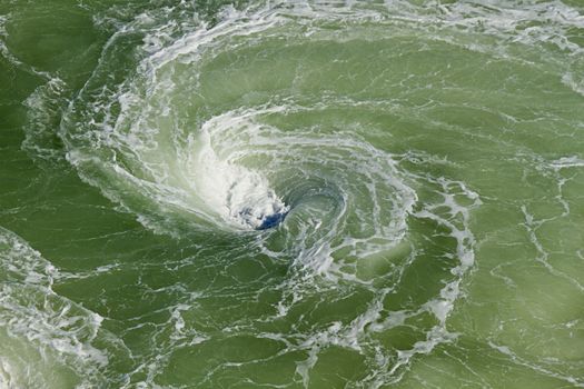 Vortex or whirlpool with foam in the river made by turning ship giving a light green color to the water