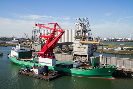 Grain elevator in harbour with terminal and cranes for transhipment and a ship getting loaded