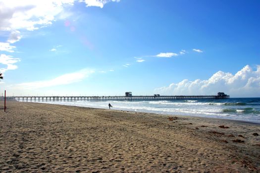 Sole Surfer walking on the Beach at Oceanside with Pier in Background