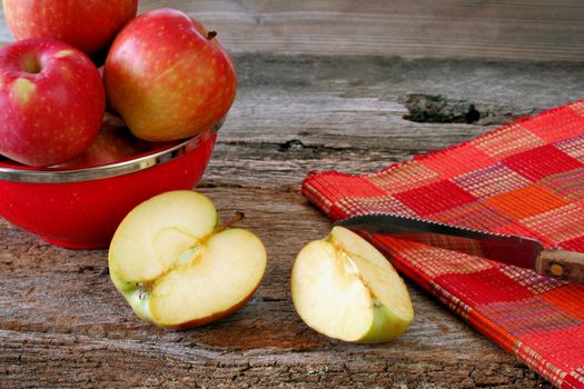 An apple that has been sliced with the knife to the side and a bowl of fresh apples in the background.