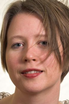 head portrait of a self confident woman with wind blown hair on light background; looking in the camera