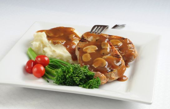 Pork chops potatoes and vegetables with mushroom gravy.