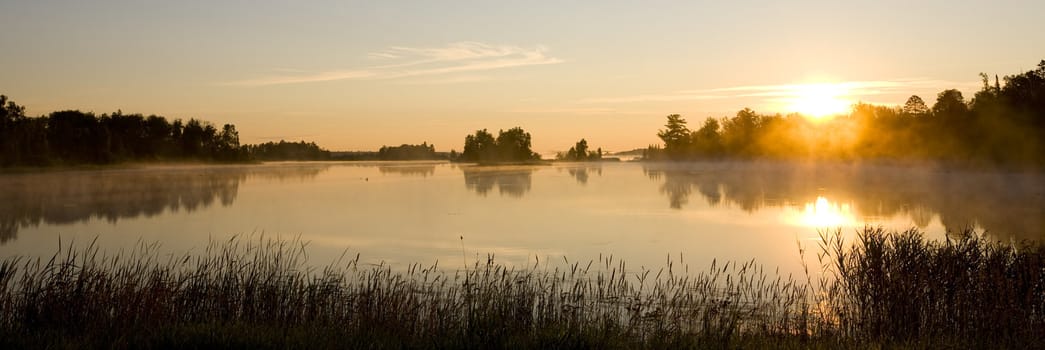 A minnesota morning as mist rolls off a small still lake.