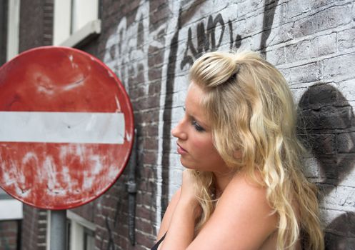 Attractive blonde against a brick wall with graffiti, standing next to a red road sign