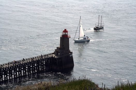 One boat coming to marine and one leaving - both are near the lighthouse built at the end of a pier. Many fishermen angling at the pier.
