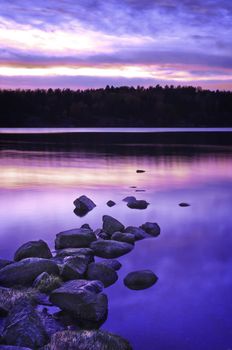 A stunning beautiful sunset over tranquil, still water. Beautiful pink, purple and blue tones with interesting rocks and shore line.