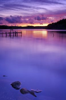 A stunning beautiful sunset over tranquil, still water. Beautiful pink, purple and blue tones with interesting rocks and shore line.