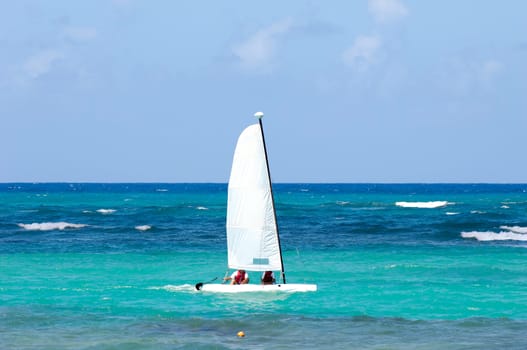 A sailboat is sailing on the blue caribbean sea.