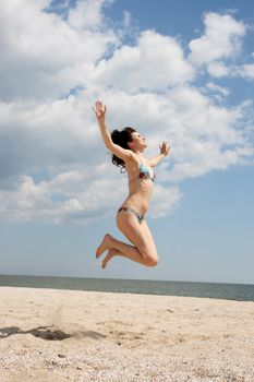 Girl jumping on the beach on the background of the sea and cloudy sky
