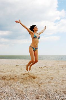 Girl jumping on the beach on the background of the sea and cloudy sky