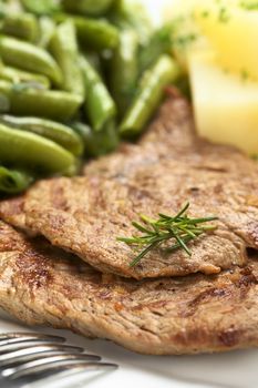Beef meat slices with fresh rosemary on top, served with green beans and cooked potatoes (Selective Focus, Focus on the front of the upper meat slice and the front of the rosemary) 