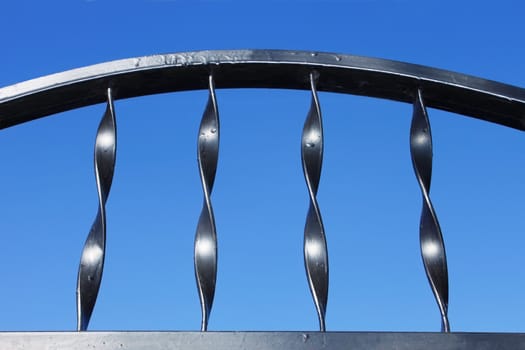 Fragment of a new painted in black metal fence against blue sky on a sunny day