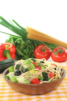 Spaghetti salad with lettuce, peppers, zucchini, olives, and green onions on a white background