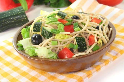 Spaghetti salad with lettuce, peppers, zucchini, olives, and green onions on a white background