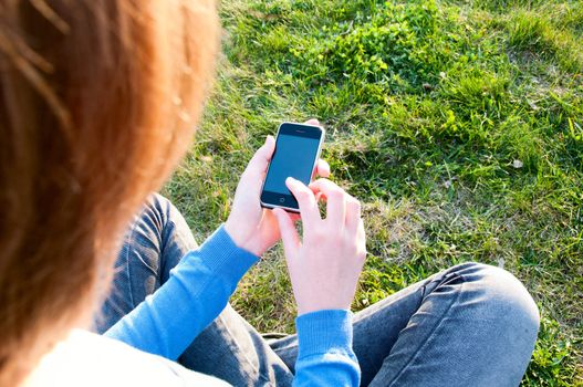 girl holding cell phone and sitting on grass