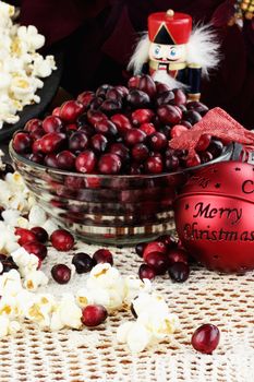 String of popcorn and cranberries with bowl of cranberries, popcorn, gift and ornaments in background. Shallow depth of field.

