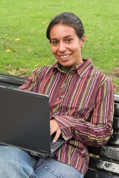 young smiling woman sitting with laptop on the bench in the park