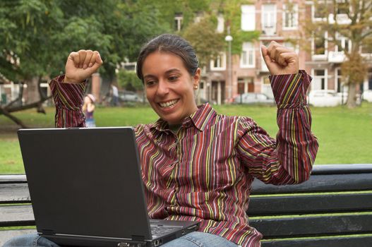 excited girl sitting on a park bench with laptop computer