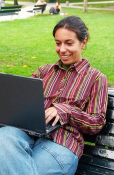 young smiling woman sitting with laptop on the bench in the park