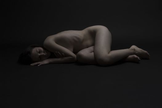Low-key studio portrait of a naked young woman resting