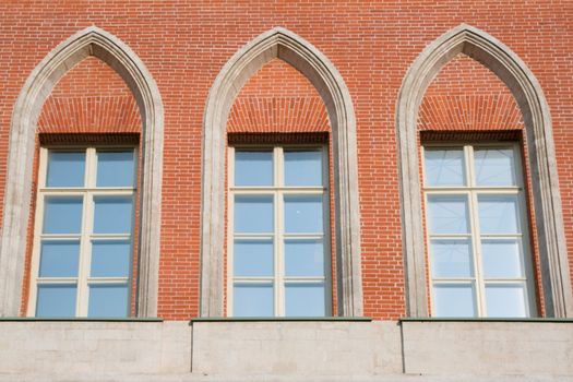 Three high glassed white-framed windows in a red brick wall